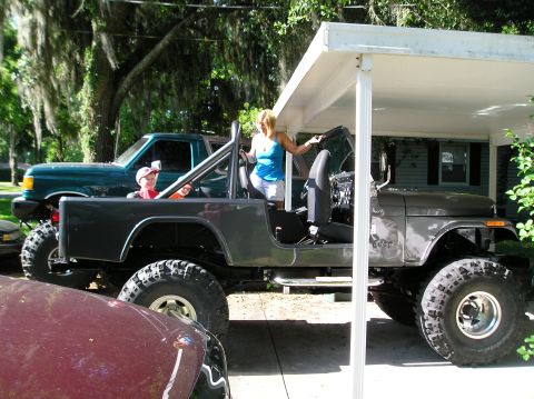 1978 Ford Bronco - A woman enters a lifted Jeep CJ-7, with a green pickup truck visible behind it.