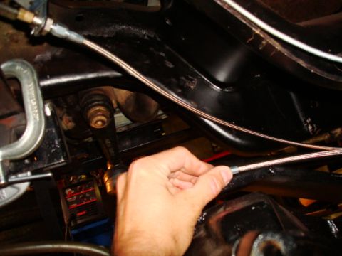 1995 Ford Bronco - A hand is shown installing a brake line on the underside of a vehicle, with a C-clamp and welding equipment visible.