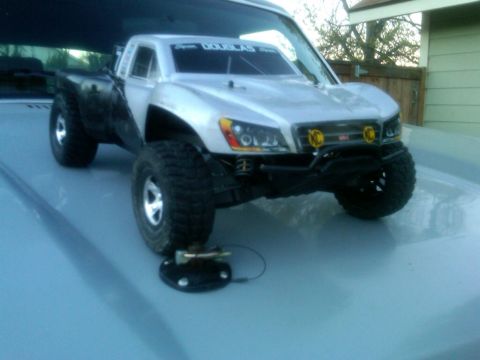 1986 Ford Bronco - A remote control truck with large tires sits on a light blue surface, with a fence and building in the background.