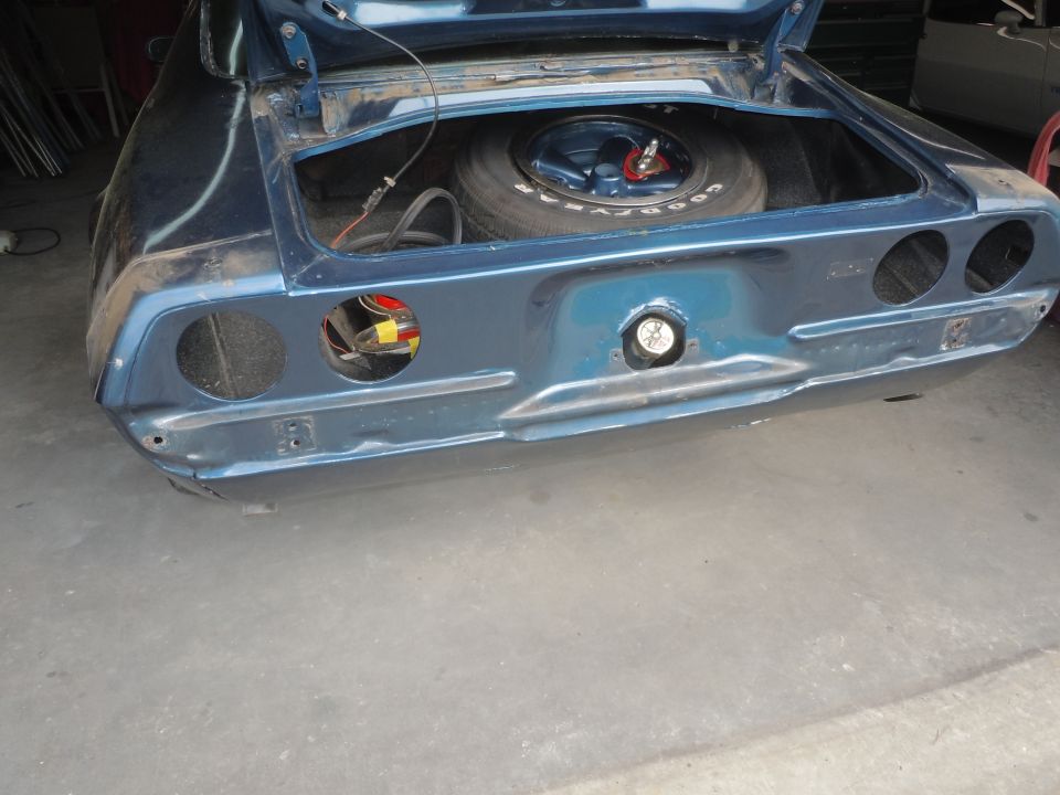 Blue car's rear with trunk open, showing spare tire and wiring. Taillight housings are empty