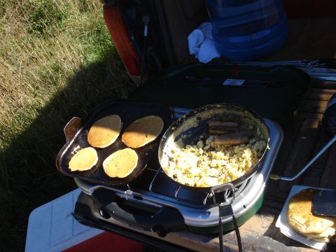 1985 Ford Bronco - Breakfast is being cooked outdoors on a portable stove, with pancakes on the griddle and sausage in a pan.