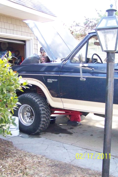 1985 Ford Bronco - A Ford Bronco is being worked on in a driveway, with its hood raised.