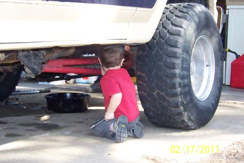 1985 Ford Bronco - A young mechanic gets hands-on experience under a lifted truck, though the vehicle's exact year and model are unconfirmed.