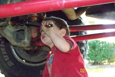 1985 Ford Bronco - A child inspects the underside of a vehicle, possibly a Ford Bronco.
