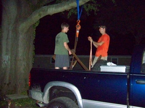 1985 Ford Bronco - Two men prepare to lift an object using a hoist attached to a tree branch, with the bed of a pickup truck visible.