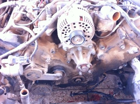 1998 Ford Crown Victoria - Close-up view of an engine, likely during a timing arms replacement, showing the alternator and water pump assembly.