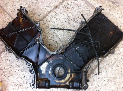 1998 Ford Crown Victoria - Engine timing cover, likely from a V-engine, with oil residue and zip ties.