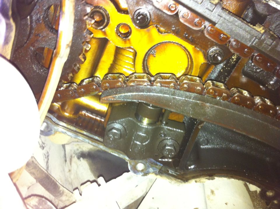 Close-up of engine timing chain, gears, and tensioner assembly. Oily metal parts