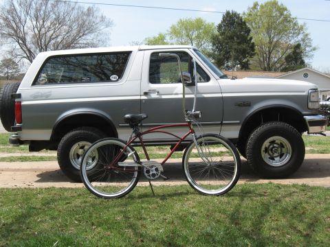 1994 Ford Bronco - A vintage Ford Bronco is parked next to a classic cruiser bicycle on a sunny day.