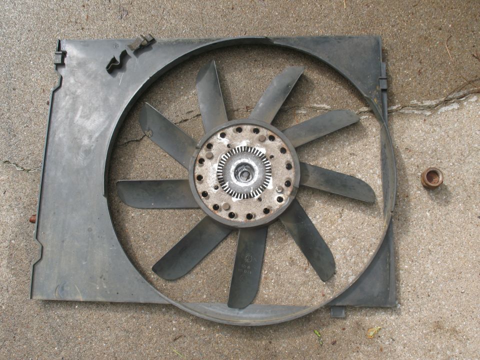 Black engine cooling fan with clutch hub and shroud lying on concrete pavement