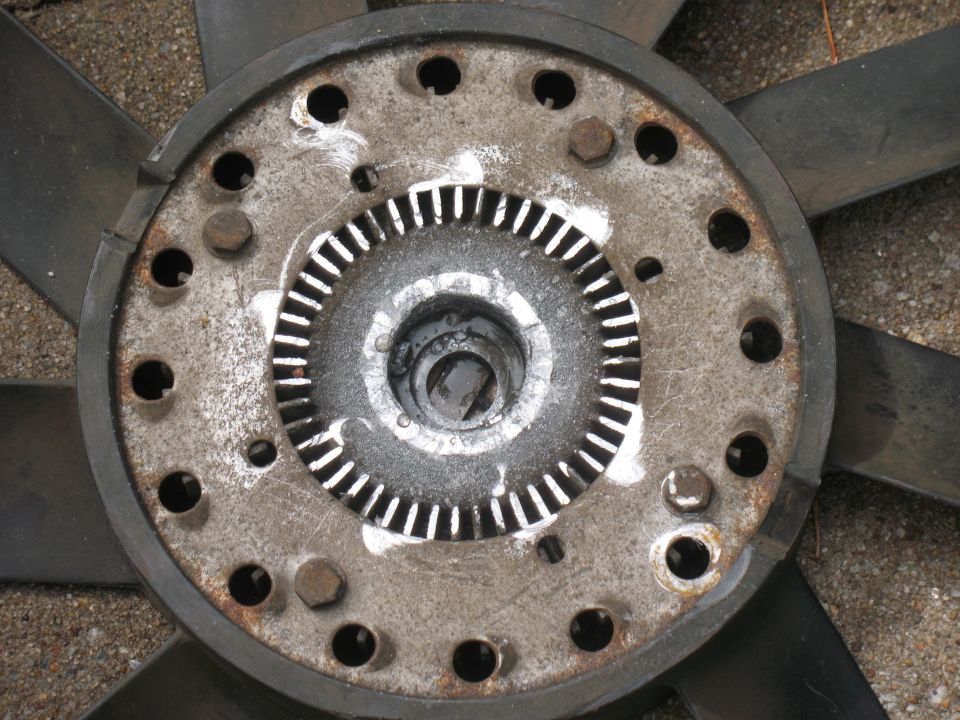 Close-up of a rusty fan clutch hub on a black plastic engine cooling fan lying on gravel