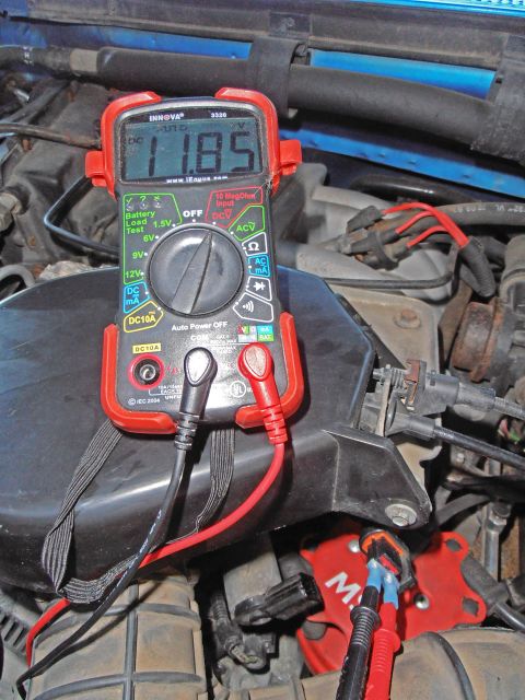 1990 Ford Bronco - A digital multimeter is shown measuring voltage within the engine bay of a vehicle.