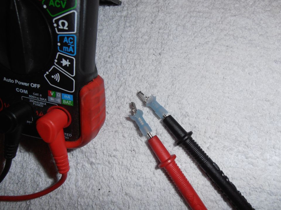 Digital multimeter with red and black test leads on a white towel