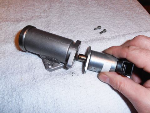 1990 Ford Bronco - A hand holds a disassembled metal automotive part with a connector and two screws on a white cloth surface.