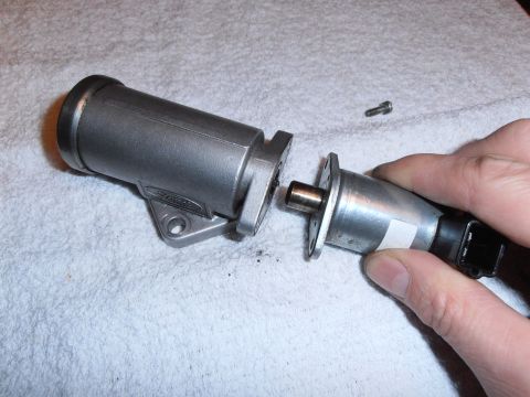 1990 Ford Bronco - A hand holds an idle air control valve assembly, which is being separated from its mounting bracket.