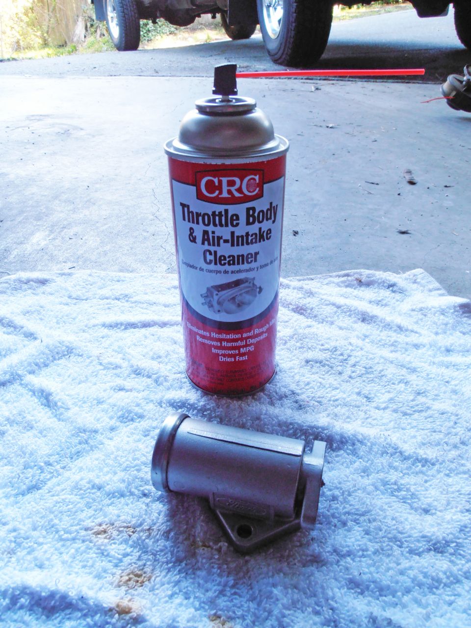 Can of CRC Throttle Body & Air-Intake Cleaner and a metal part on a towel, with part of a vehicle in the background