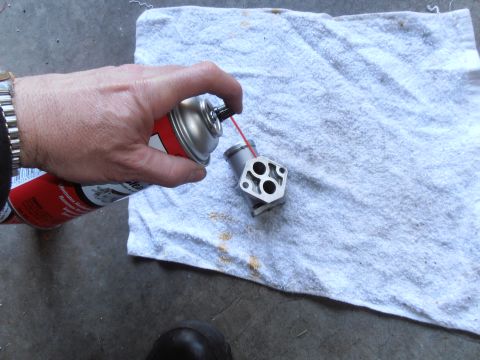 1990 Ford Bronco - A hand sprays a throttle body part with cleaner. The part is resting on a white towel.