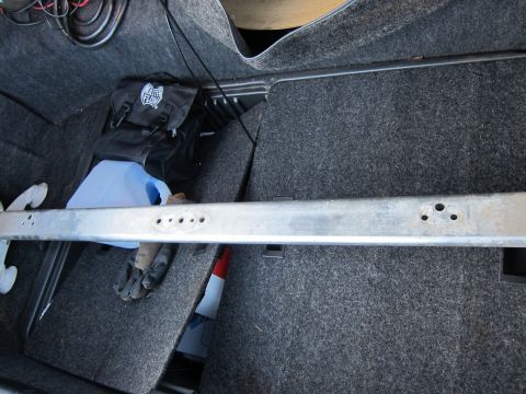 1991 Ford LTD Crown Victoria - The interior of a vehicle's trunk is shown, a metal bar across the frame and various items including a black bag and a blue container.