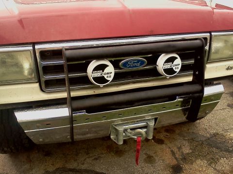 1989 Ford Bronco - Front view of a red Ford Bronco with a bull bar and winch, showing Pro Comp lights on the grille.
