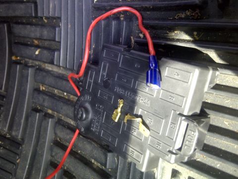 2000 Ford Crown Victoria - Close-up of a vehicle fuse box with a red wire and a blue connector attached.