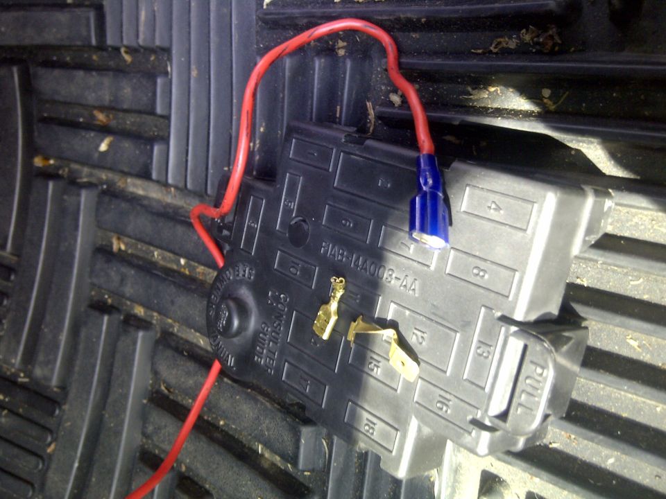 Automotive fuse box with a red wire connected via a blue butt connector. Part number F1AB-14A003-AA is visible
