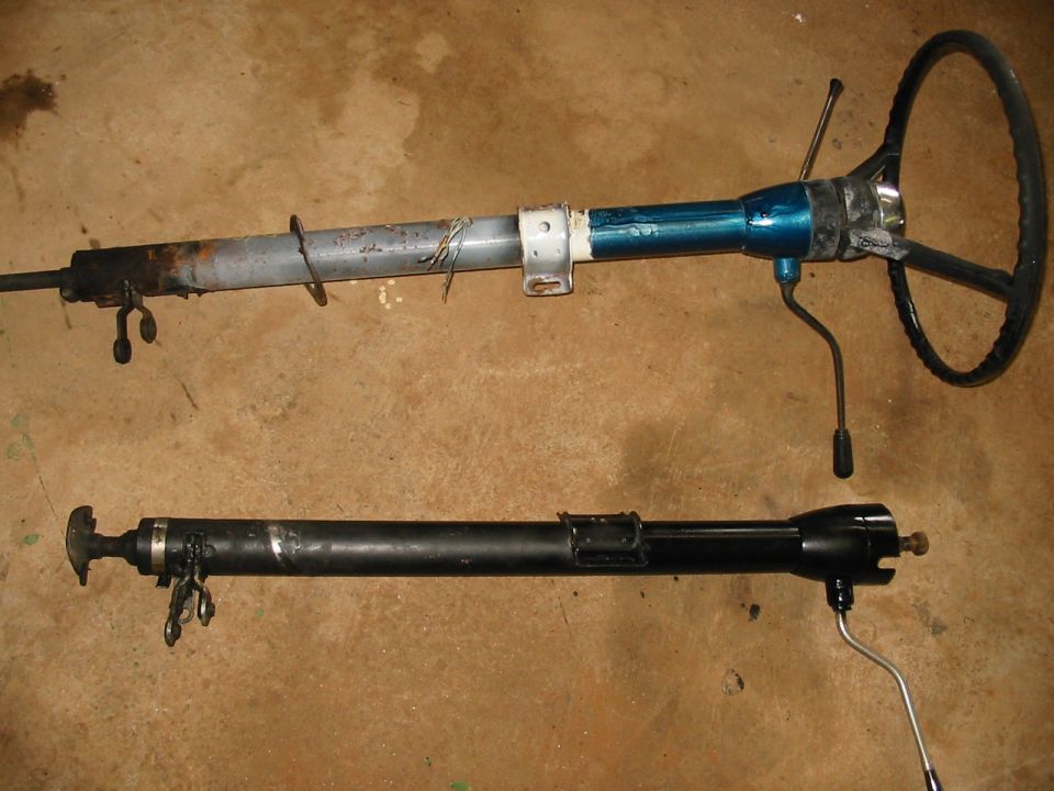 Two steering columns, one blue and rusty, the other black, lie on a concrete floor