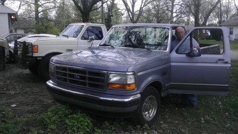 1989 Ford Bronco - A blue 1992 Ford F-150 pickup truck is parked next to a white truck, with a man standing in the open driver's door.