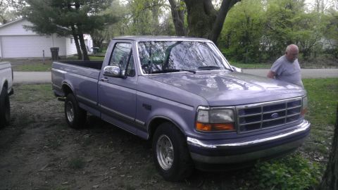 1989 Ford Bronco - A man leans on the hood of a 1992 Ford F-150 pickup truck parked in a yard.