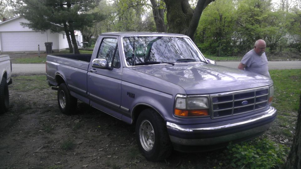 1992 Ford F-150 pickup truck parked outside with a man leaning on the hood