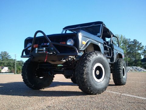 1967 Ford Mustang - Low three-quarter front shot of a heavily lifted black early Ford Bronco with the top removed, wearing an exposed roll cage, tubular front…