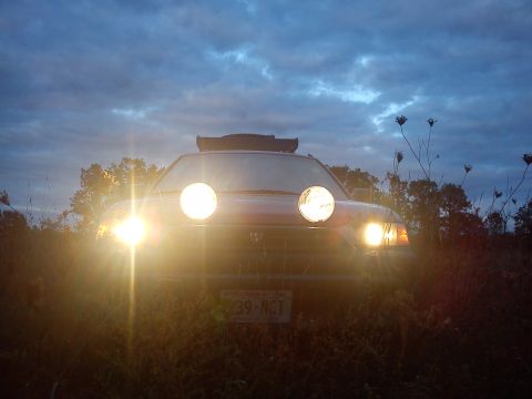 1998 Subaru Legacy - A red 1998 Subaru Legacy is parked outdoors at dusk, its headlights and auxiliary lights illuminating the surroundings.