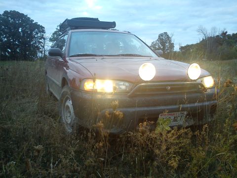 1998 Subaru Legacy - This 1998 Subaru Outback is equipped with a roof rack and auxiliary fog lights, seen here in a grassy, outdoor setting.