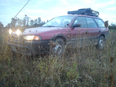 1998 Subaru Legacy - Red 1998 Subaru Outback with roof rack and auxiliary lights sits in tall grass.