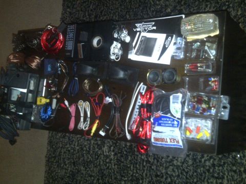 2000 Ford Crown Victoria - Various car audio components and installation supplies are spread out on a dark surface.