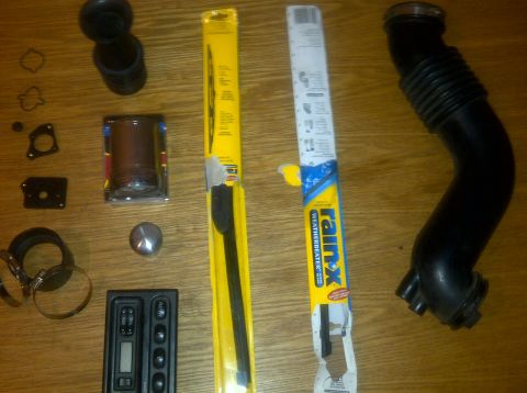 2000 Ford Crown Victoria - A collection of automotive parts laid out on a wooden surface, including an air intake hose and windshield wipers.
