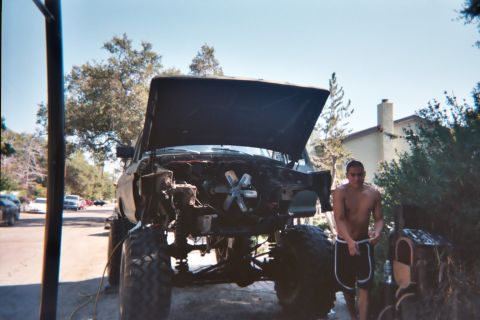 1978 Ford Bronco - A shirtless man stands beside a custom truck undergoing modifications, with the engine compartment fully visible.