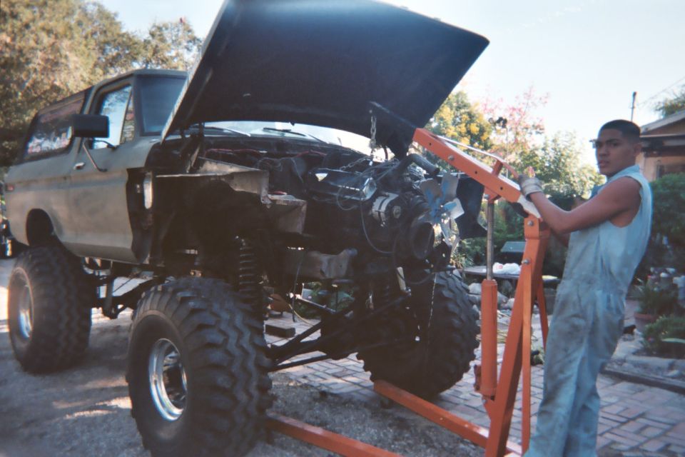 Tan lifted Ford 4x4 with V8 engine hanging from an orange hoist during an engine swap