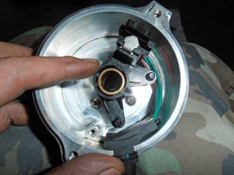 1990 Ford Bronco - Hand pointing at the inside of a distributor base, brass shaft bushing and black ignition pickup with green wire.