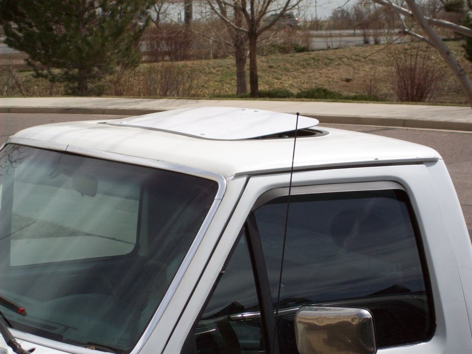 White truck sunroof partially open, chrome trim, antenna, reflection in side mirror