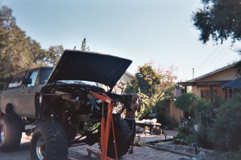 Lifted Ford 4x4 with hood open and orange engine hoist over the engine bay in a driveway