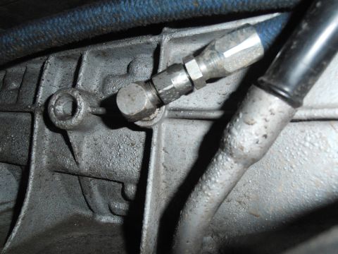 1990 Ford Bronco - A close-up view of a metal fitting connecting a blue hose to a vehicle's transmission housing.