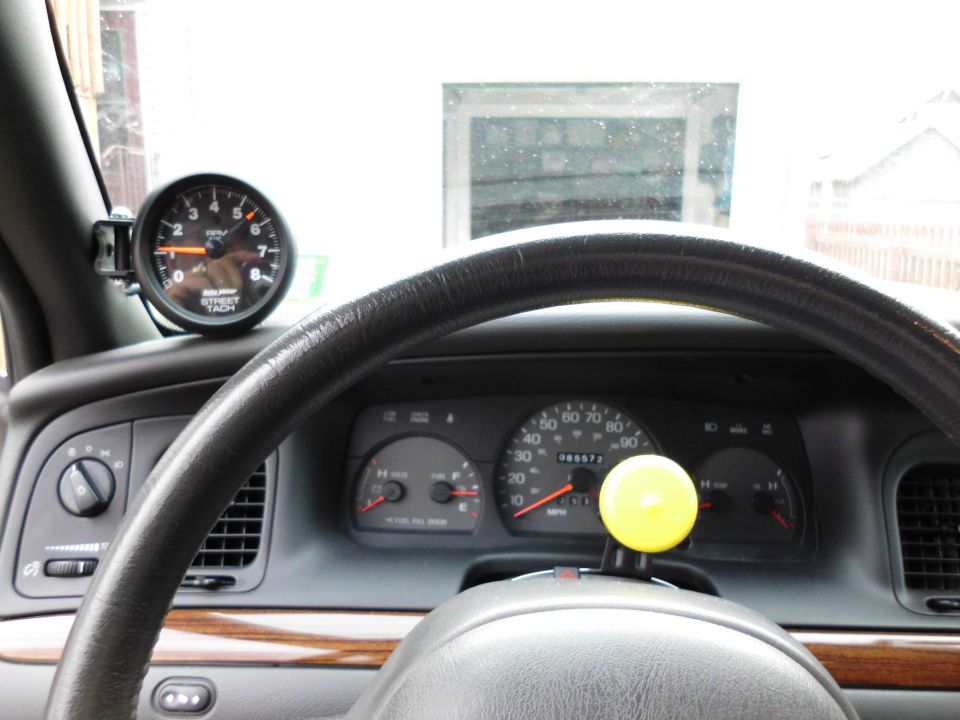 Interior view of gauge cluster and steering wheel with yellow spinner knob and A-pillar-mounted Auto Meter Street Tach
