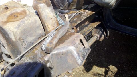 1978 Ford Bronco - Close-up of heavily rusted vehicle suspension components being cleaned with a wire brush.