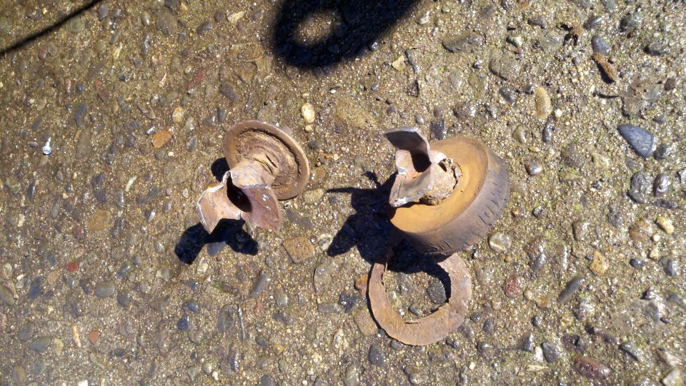 Two broken metal pieces and a fragment of a tire on a gravelly surface