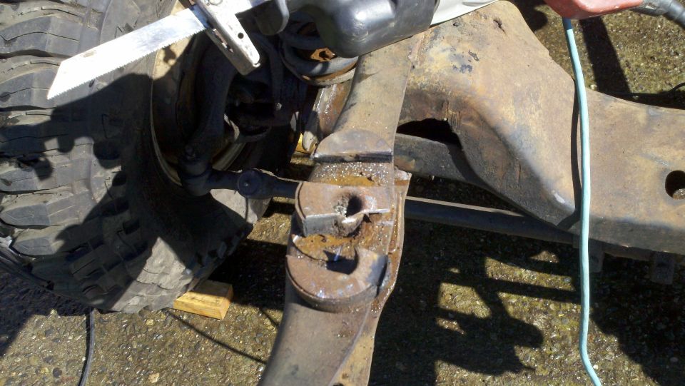 Close-up of a rusty metal suspension component being cut by a reciprocating saw near a large tire