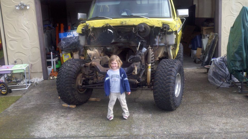 kid in front of yellow truck with front end removed, lifted suspension, big tires