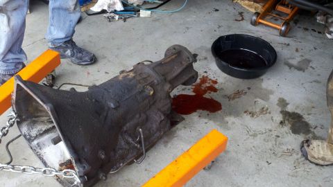 1978 Ford Bronco - Transmission removed from vehicle, resting on an engine stand with a drain pan nearby.