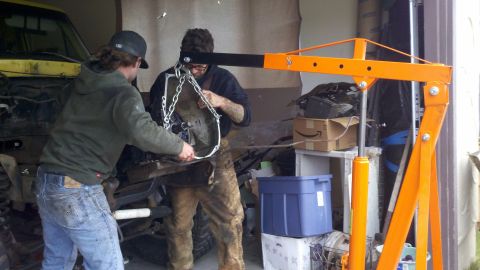 1978 Ford Bronco - Two mechanics are working on removing a transmission from a vehicle using an engine hoist.