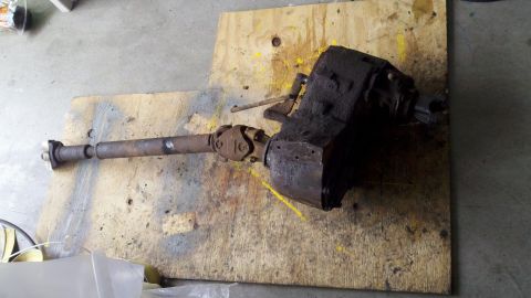 1978 Ford Bronco - A greasy transfer case and driveshaft assembly rests on a piece of plywood.