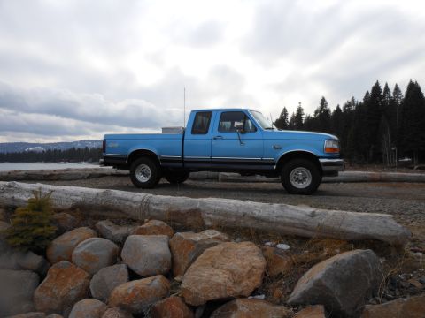 1992 Ford F-150 - A blue 1992 Ford F-150 pickup truck is parked on a gravel road next to a body of water.